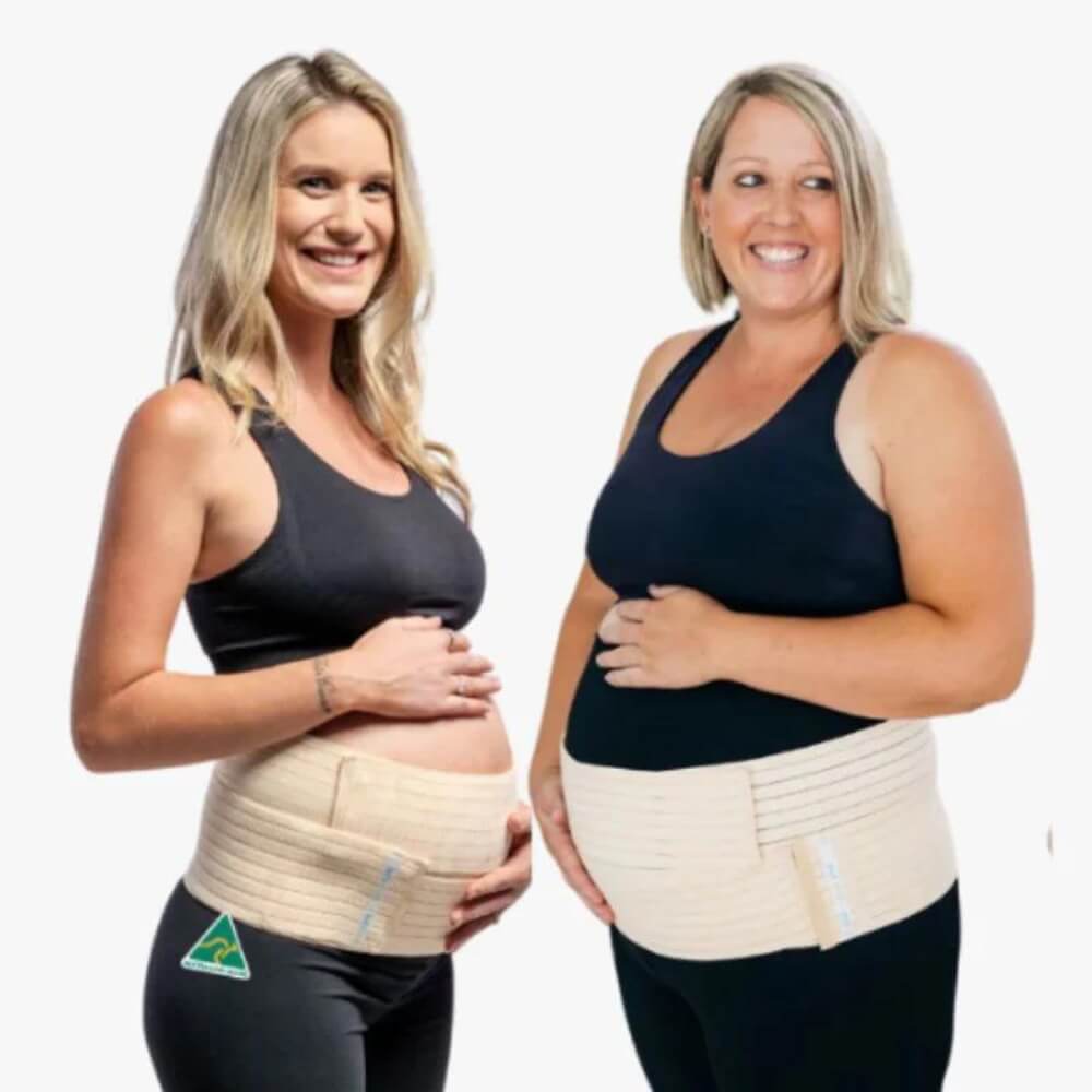 Two pregnant women stand side by side, smiling and looking at each other. They both wear black tank tops and beige Belly Bands 3-in-1 Belly Bands for Pregnancy, Postpartum, C-section over their baby bumps, showcasing essential pregnancy care. The background is plain white.