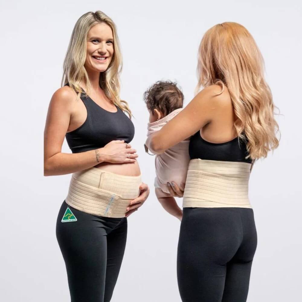 Two women are wearing black workout attire and beige 3-in-1 Belly Bands for Pregnancy, Postpartum, C-section by Belly Bands. The woman on the left is pregnant, smiling with her hand on her belly. The woman on the right is showcasing pregnancy care while holding a baby with her back to the camera. Both are set against a plain white background.