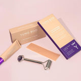 The C-Section Scar Bundle by Yung Bod features a selection of products including the C-section Rock 'N' Roller, a tube of scar cream, and a silicone strip, all smartly packaged. The roller stands out with its purple handle and textured head. Emphasizing postpartum scar care essentials, the bundle comes in beige and purple boxes filled with natural ingredients.