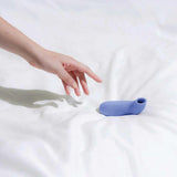 A hand reaches toward the Dame Aer - External Suction by Dame, an abstractly shaped object crafted from waterproof silicone, resting gracefully on a white surface.