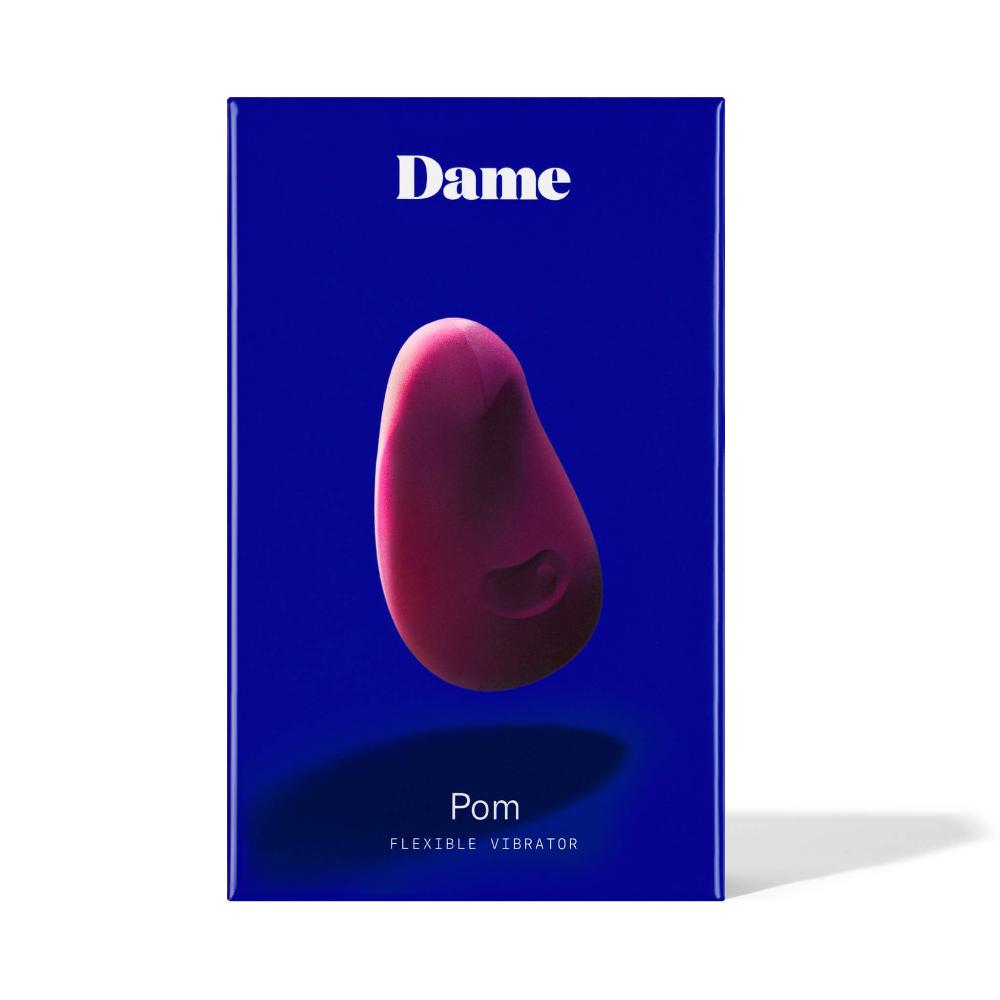 A product box displays the Dame Pom, a purple, pebble-shaped external flexible vibrator by Dame. The background is deep blue with "Dame" in white text, emphasizing its ergonomic design and medical-grade silicone for a comfortable experience.