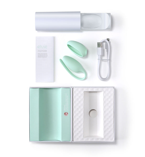 An open package reveals the Elvie Pelvic Floor Trainer by Elvie, featuring a white cylindrical case, two mint green elliptical devices, a USB charging cable, and a product manual. These items, designed for optimal pelvic health and effective Kegel exercise routines, are neatly arranged against a white background.