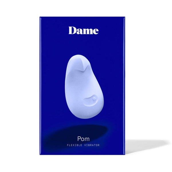 The dark blue box of the Dame Pom - External Flexible Vibrator, made from medical-grade silicone, is displayed elegantly against a white background. A sleek white image of the product is featured in the center with "Dame Pom - External Flexible Vibrator" printed prominently on it.