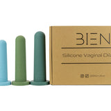 A set of four silicone vaginal dilators in soothing colors (light blue, blue, green, dark green) stand beside a cardboard box labeled 