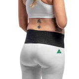 A woman sporting a white sports bra and pants complements her outfit with the Belly Bands Maternity Sacroiliac Pelvic Support Belt in black around her waist. Her back and side tattoos add flair, while the pants feature a small green triangle logo.