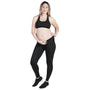 A pregnant person is standing and smiling, wearing a black sports bra, SRC maternity Leggings by SRC Health in black, and dark sneakers. They have one hand resting on their abdomen and the other by their side. The background is plain white.