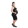 A pregnant woman stands smiling, wearing a black sports bra and SRC Health's SRC Pregnancy Shorts - Over the Bump, which provide pelvic support. She has one hand resting on her belly and complements her look with black sneakers. The background is plain white.