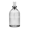 The Uberlube silicone lubricant is housed in a sophisticated clear glass bottle featuring a sleek white pump dispenser. Its minimalistic, modern design conceals the liquid within, while the lowercase "Uberlube" brand name elegantly adorns the front, exemplifying sophistication and versatility in sexual wellness.